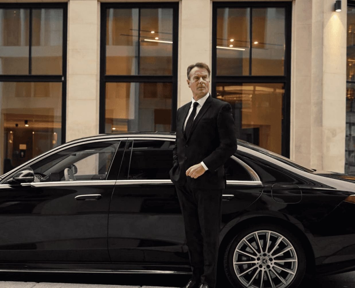 A LuxLane chauffeur in a dark suit beside a Mercedes sedan